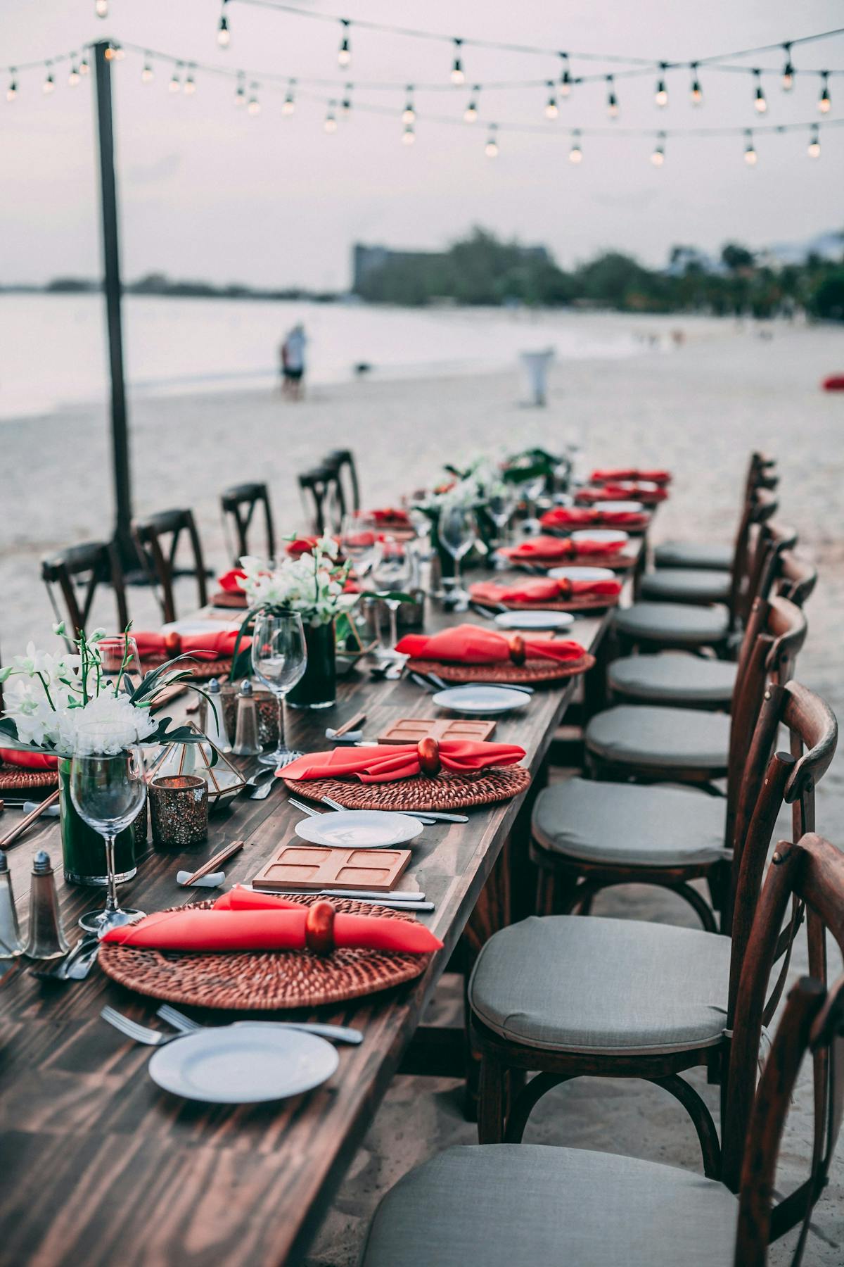  A long beach table adorned with red and white place settings, creating a festive dining atmosphere by the ocean