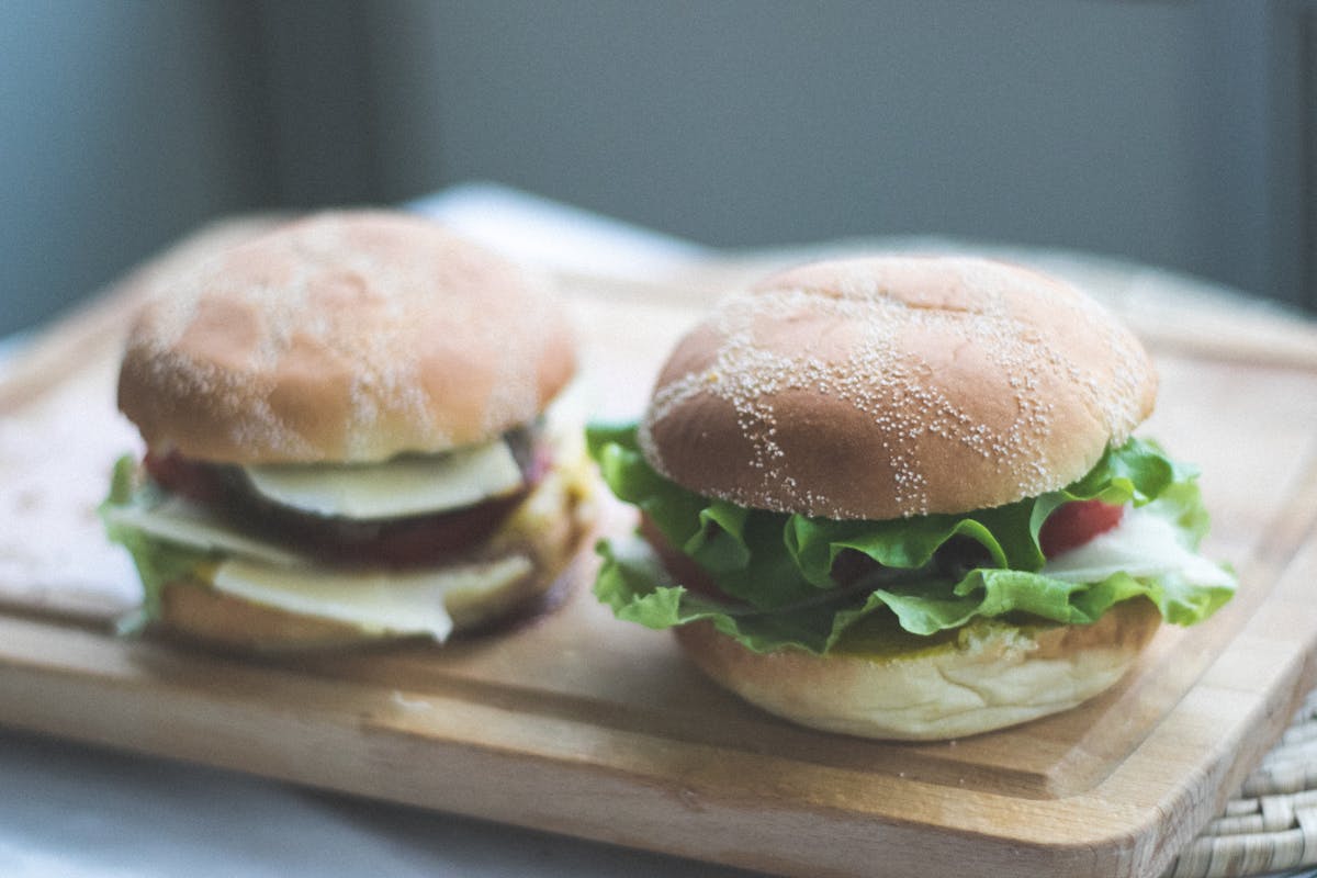 Two hamburgers with lettuce and tomato placed on a wooden cutting board