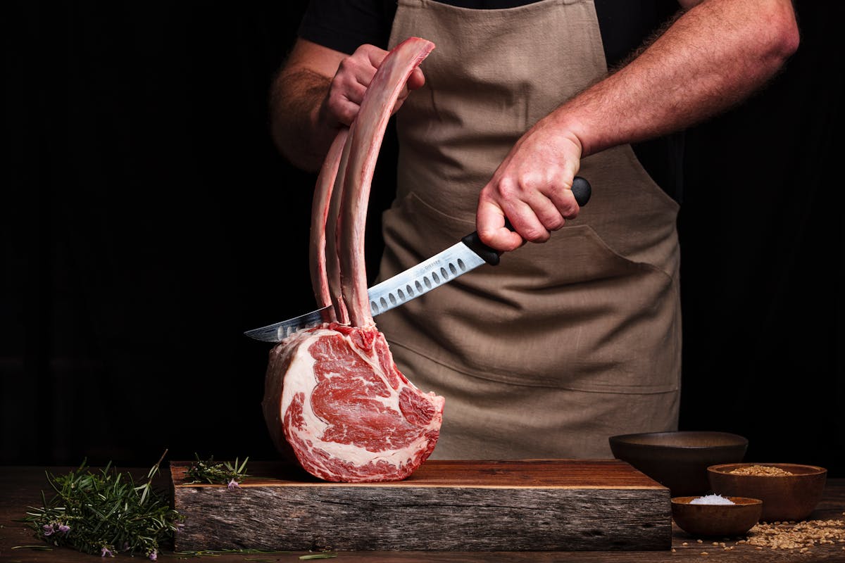 a photo of a man cutting a piece of meat on a butcher block