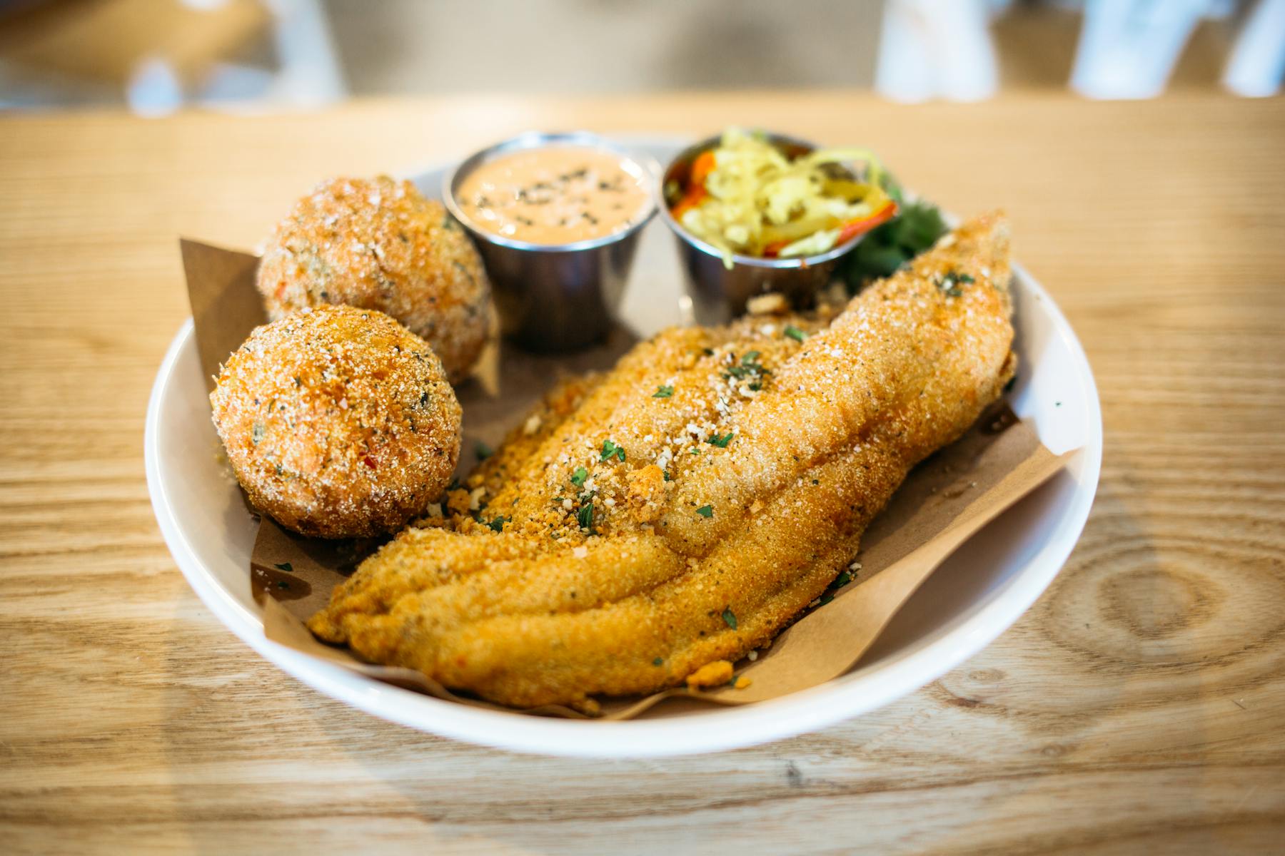 a plate topped with fried fish, biscuits, coleslaw salad sitting on a wooden table