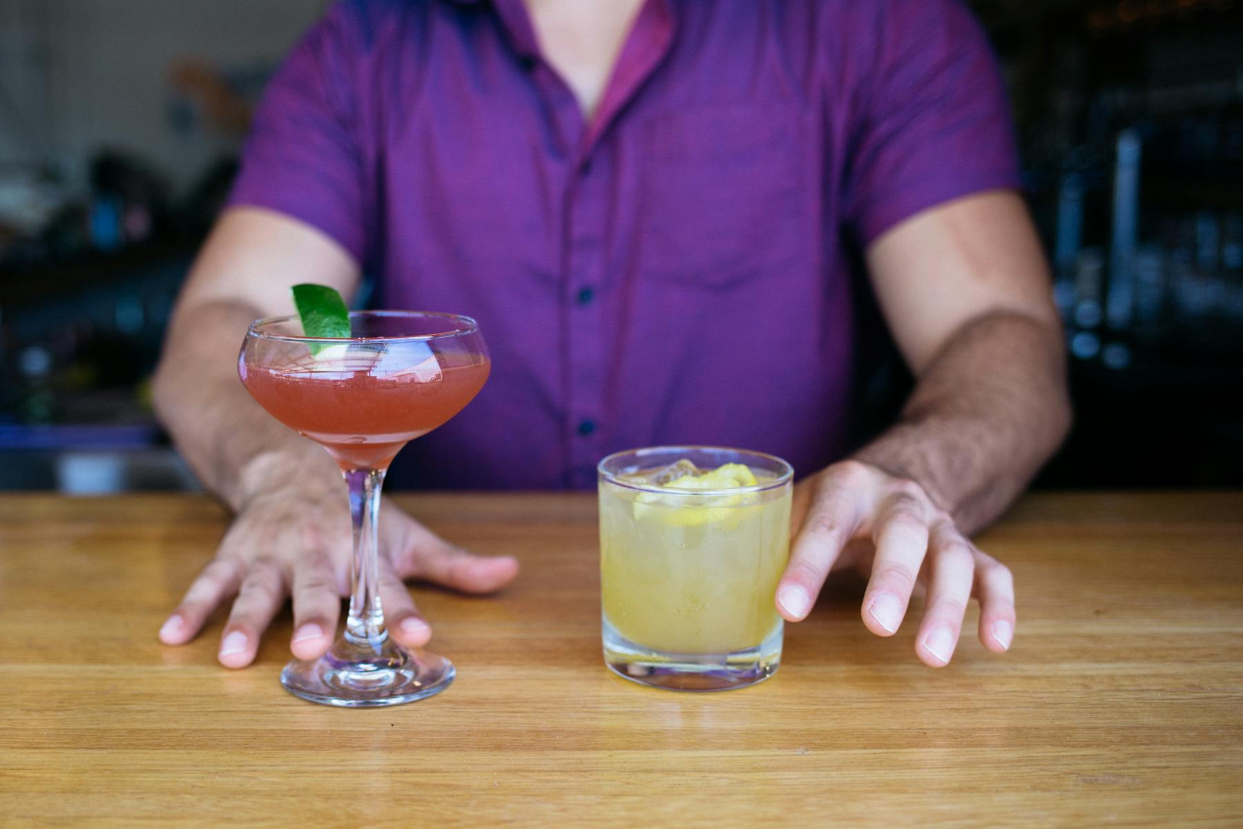 a person sitting at a table with a cocktail and a lemonade
