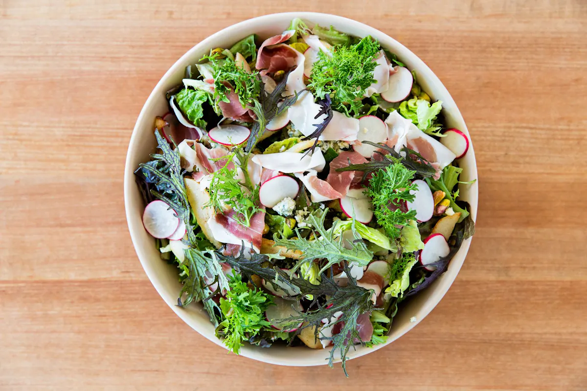 a bowl of salad sitting on top of a wooden table