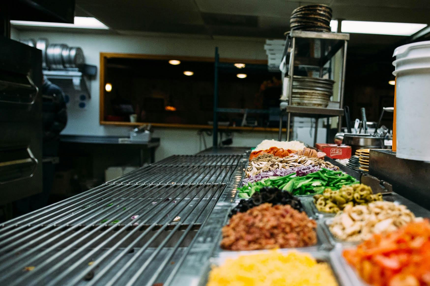 the ingredients for making a pizza lined up on a tray and the kitchen as the background