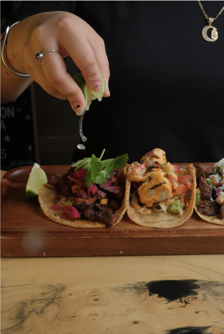 Lime getting squeezed on top of a taco on a tray of tacos