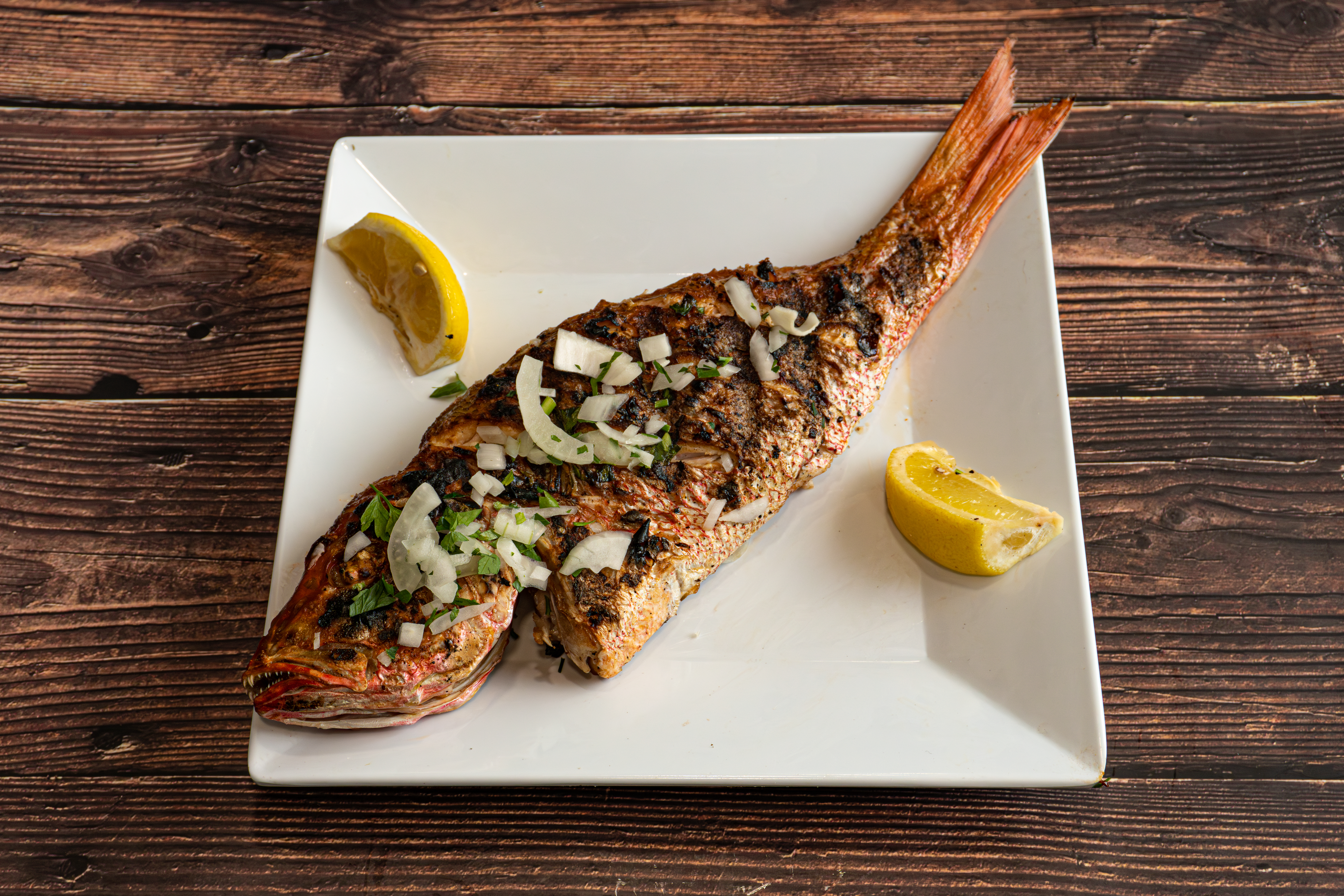 a fish on a plate with lemon wedges