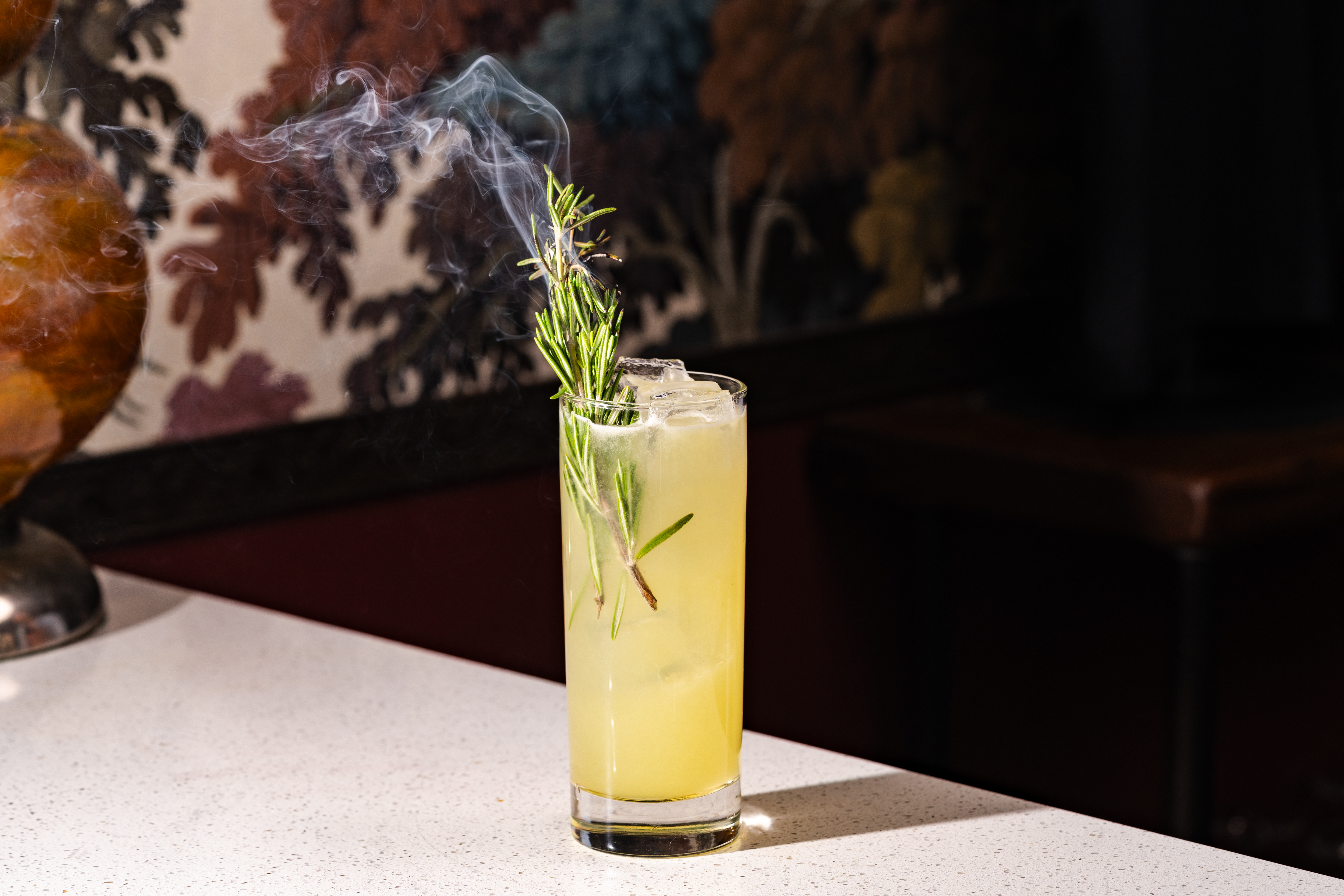 a glass with a drink and a sprig of rosemary