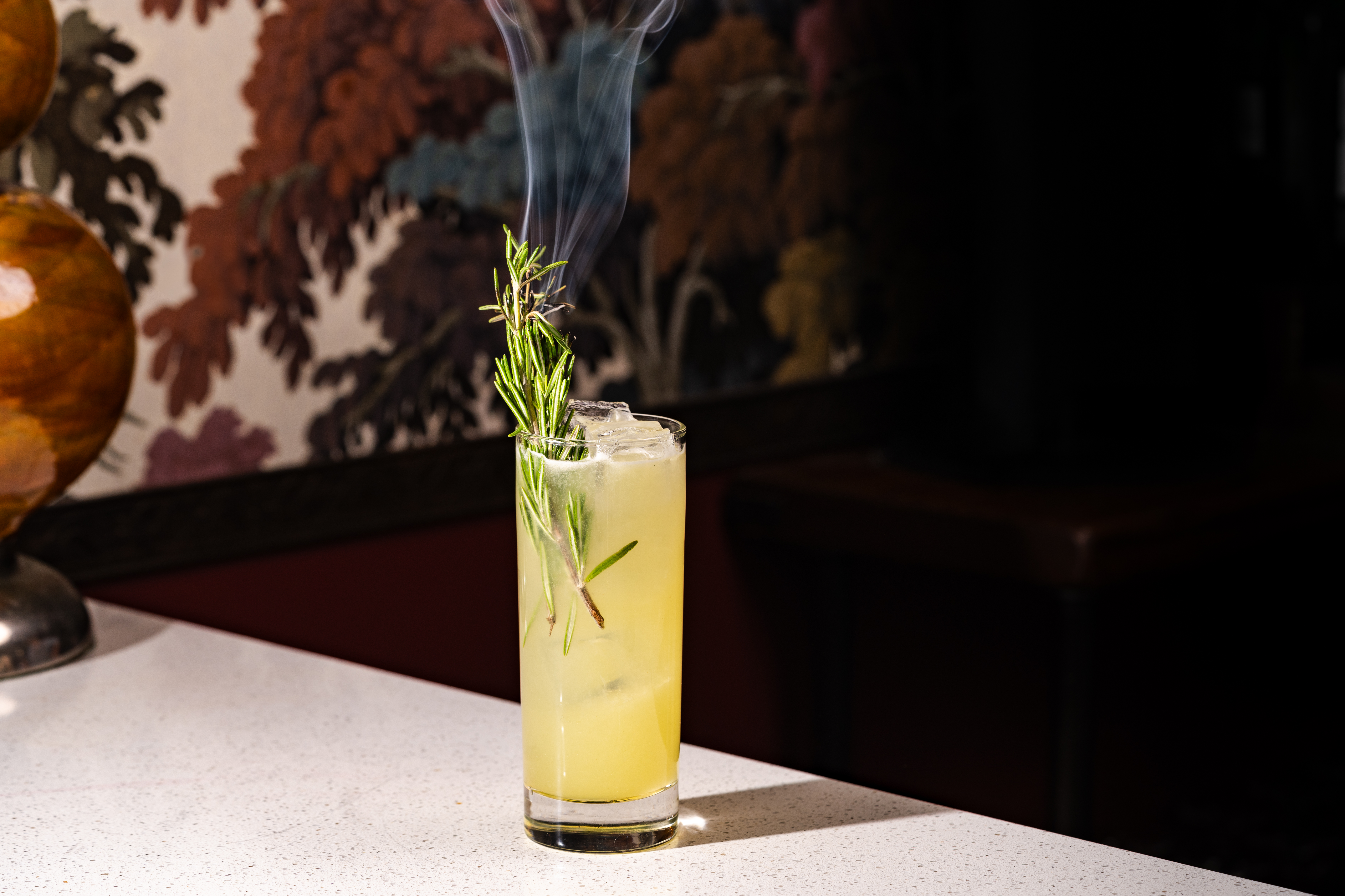 a glass with a drink and a sprig of rosemary