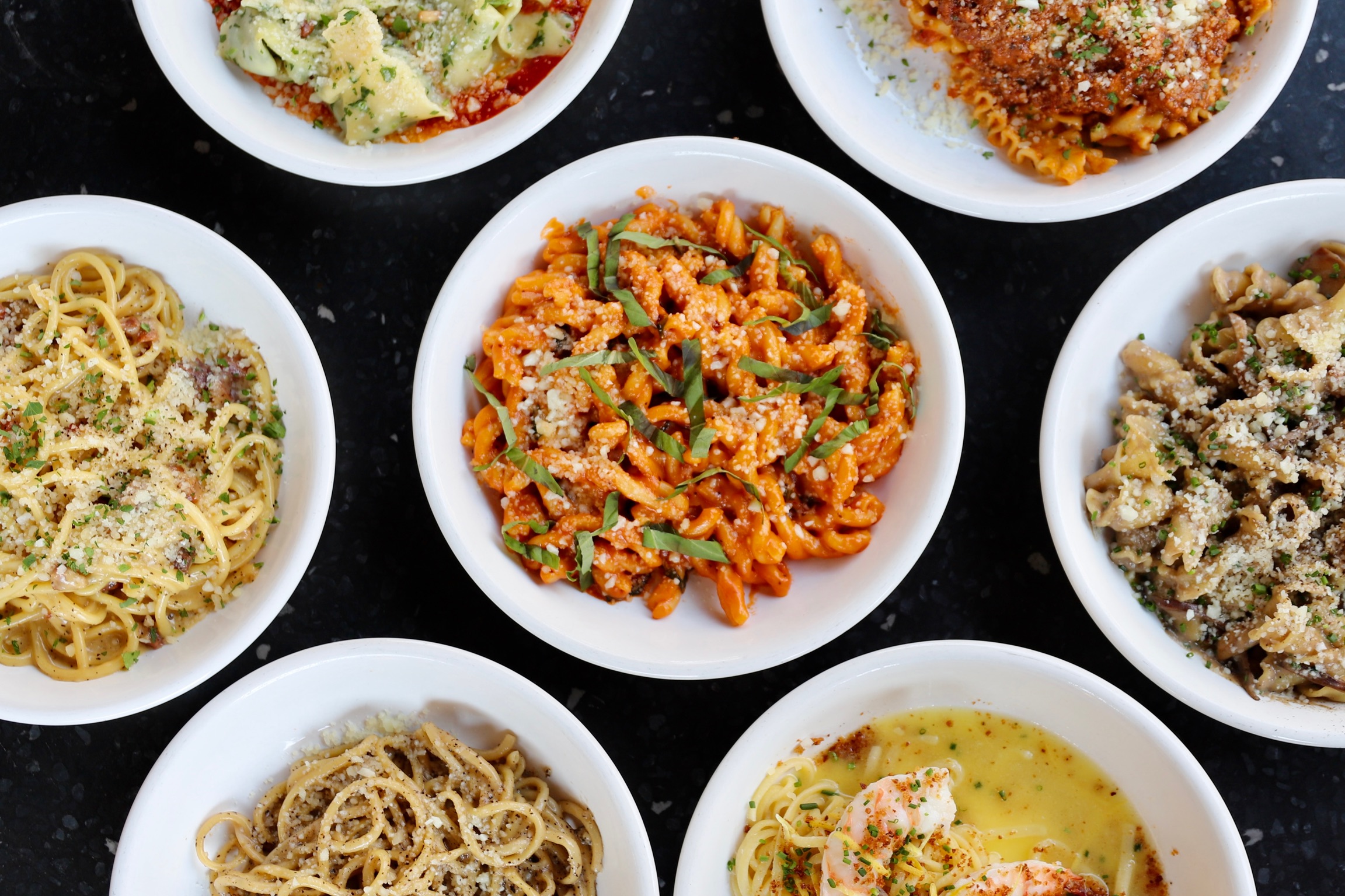 a bowl of pasta with many different types of food on a table