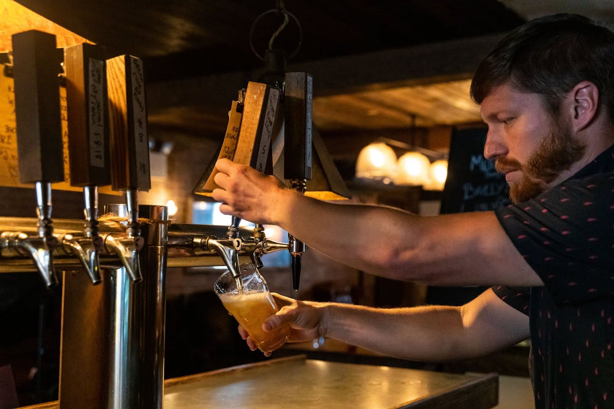 A man pouring a beer from the tap at a bar.