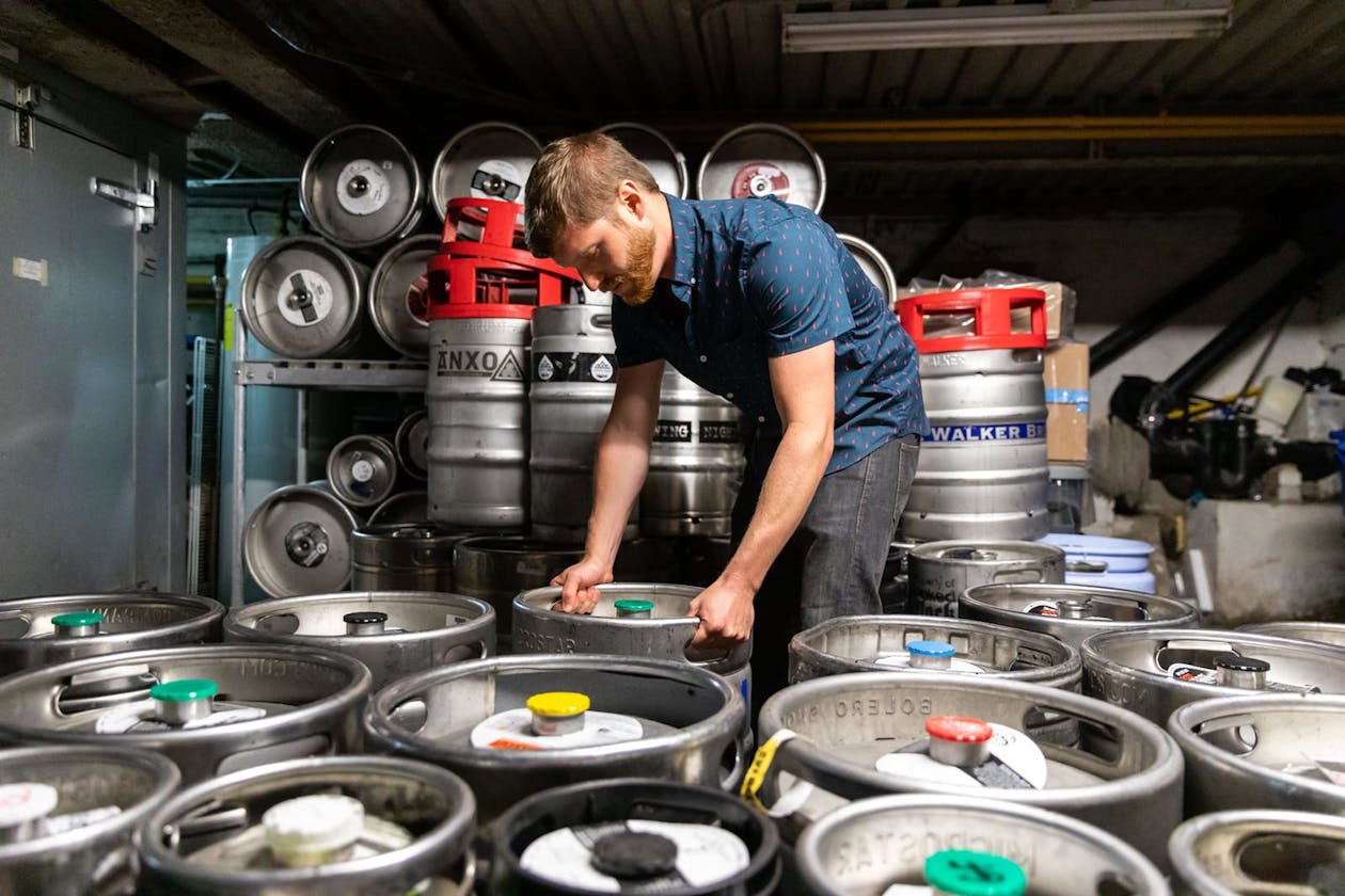 A man organizing kegs of beer in a basement.