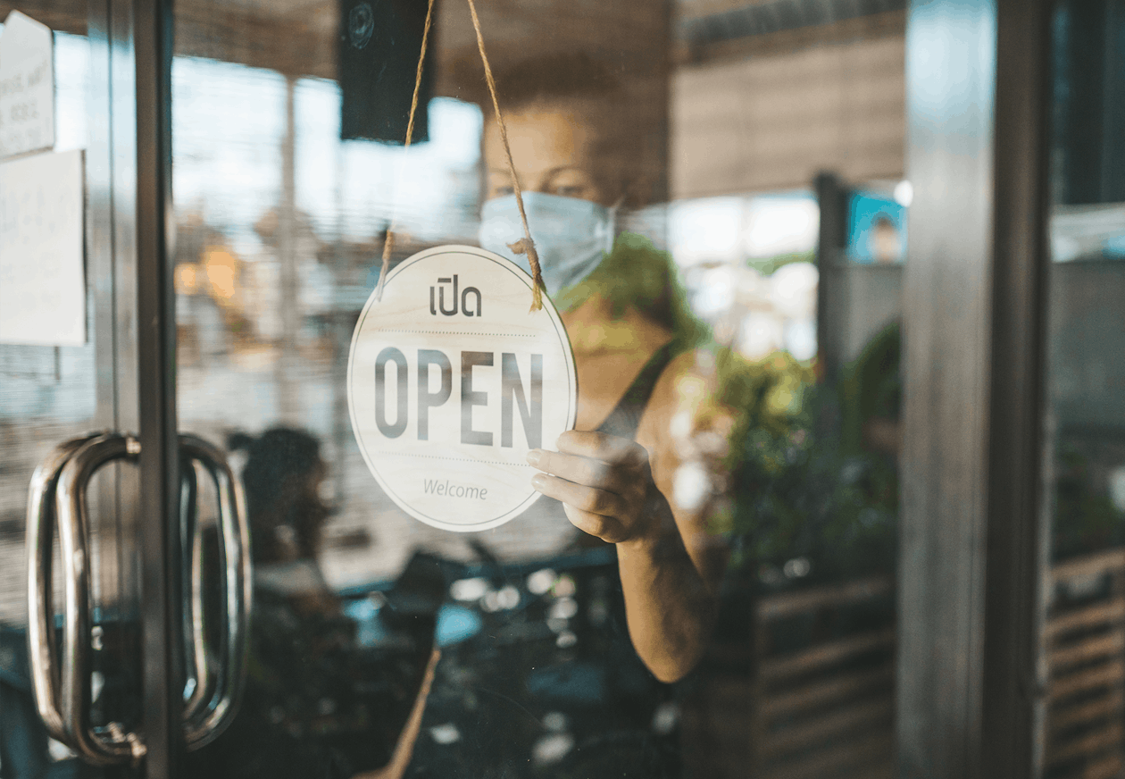 Restaurant owner wearing a face mask holding an OPEN sign at their door