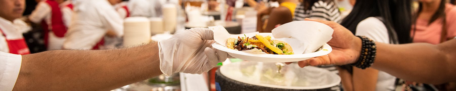 Food hall staff handing a plate of tacos to a customer over the counter