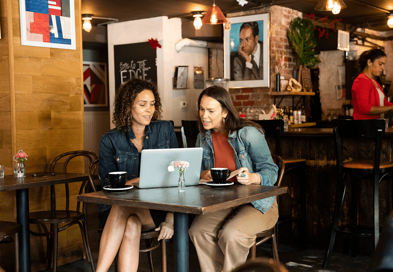 two people sitting at a table in a restaurant looking at a computer screen