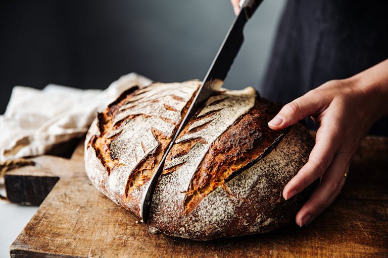 Baker cutting into a loaf of bread