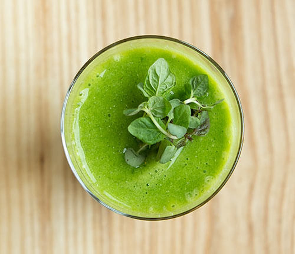 a glass of green juice sitting on top of a wooden table