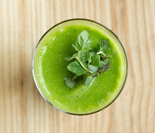 a glass of green juice sitting on top of a wooden table