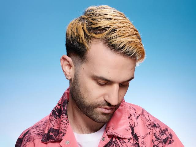 A portrait of a man with short bleached-blonde hair and a trimmed beard