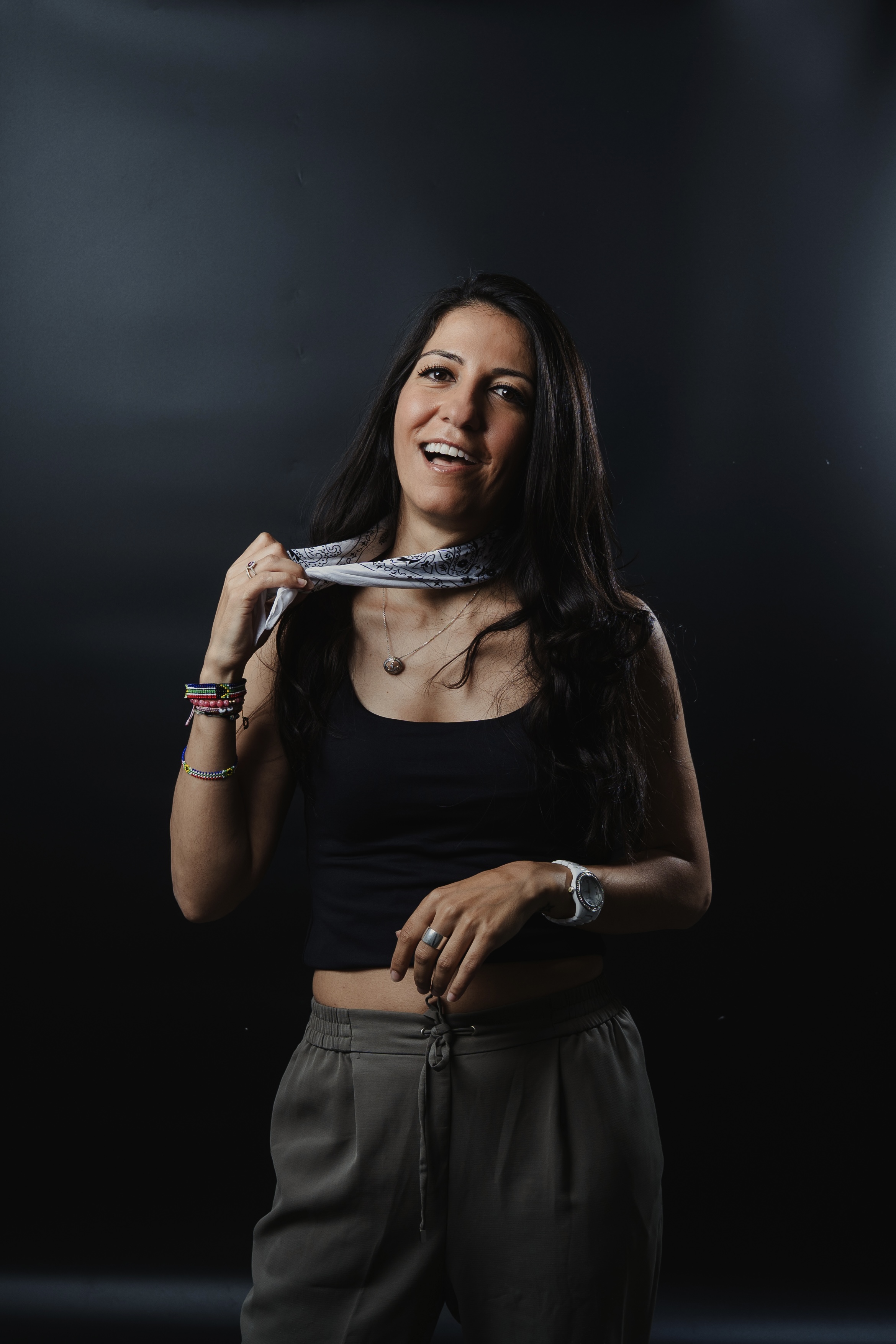 Portrait of a smiling woman in casual attire holding a bandana, set against a dark backdrop