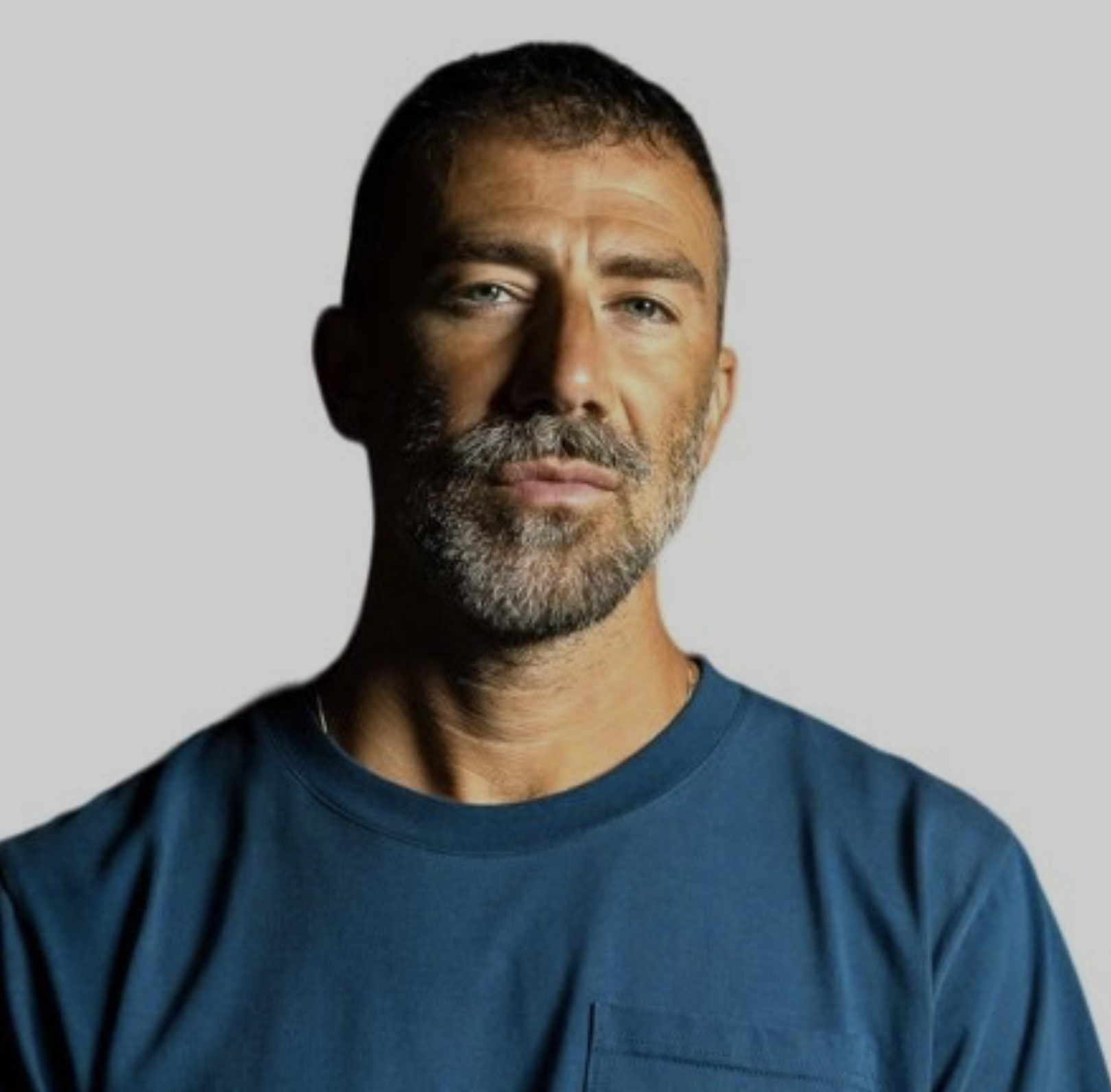 Studio headshot of a middle-aged man with a grey beard and short hair