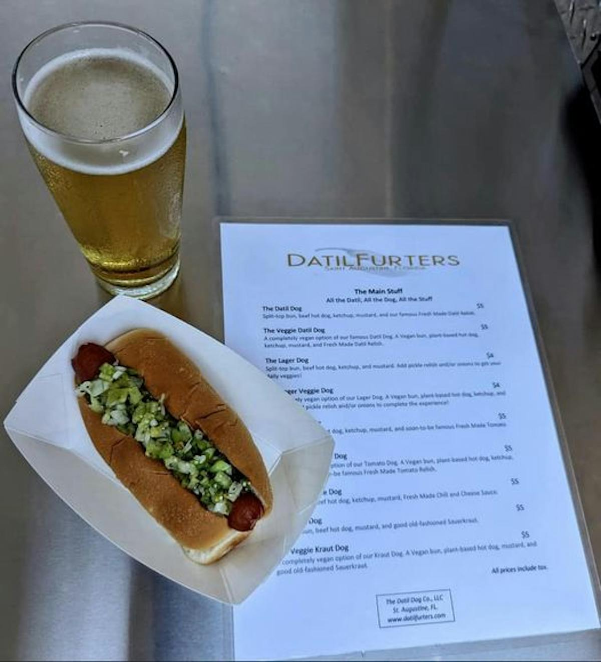 a hot dog next to a glass of beer on a table