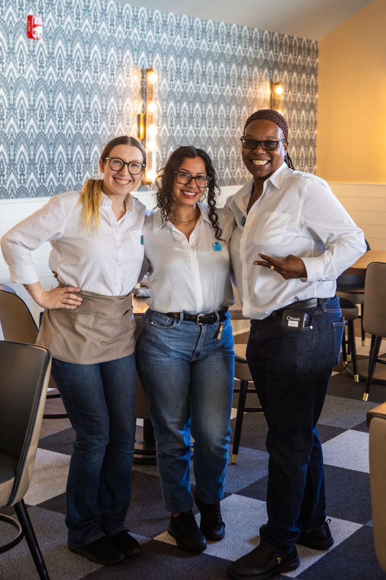 Three servers smiling and posing together wearing their Crosby's Kitchen uniforms