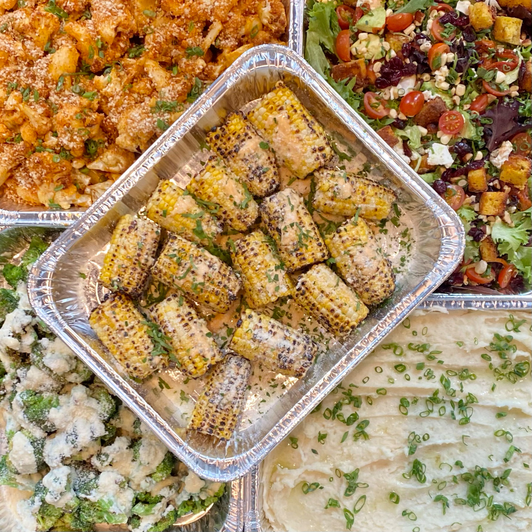 Four catering pans with a pan of corn resting on top in the center