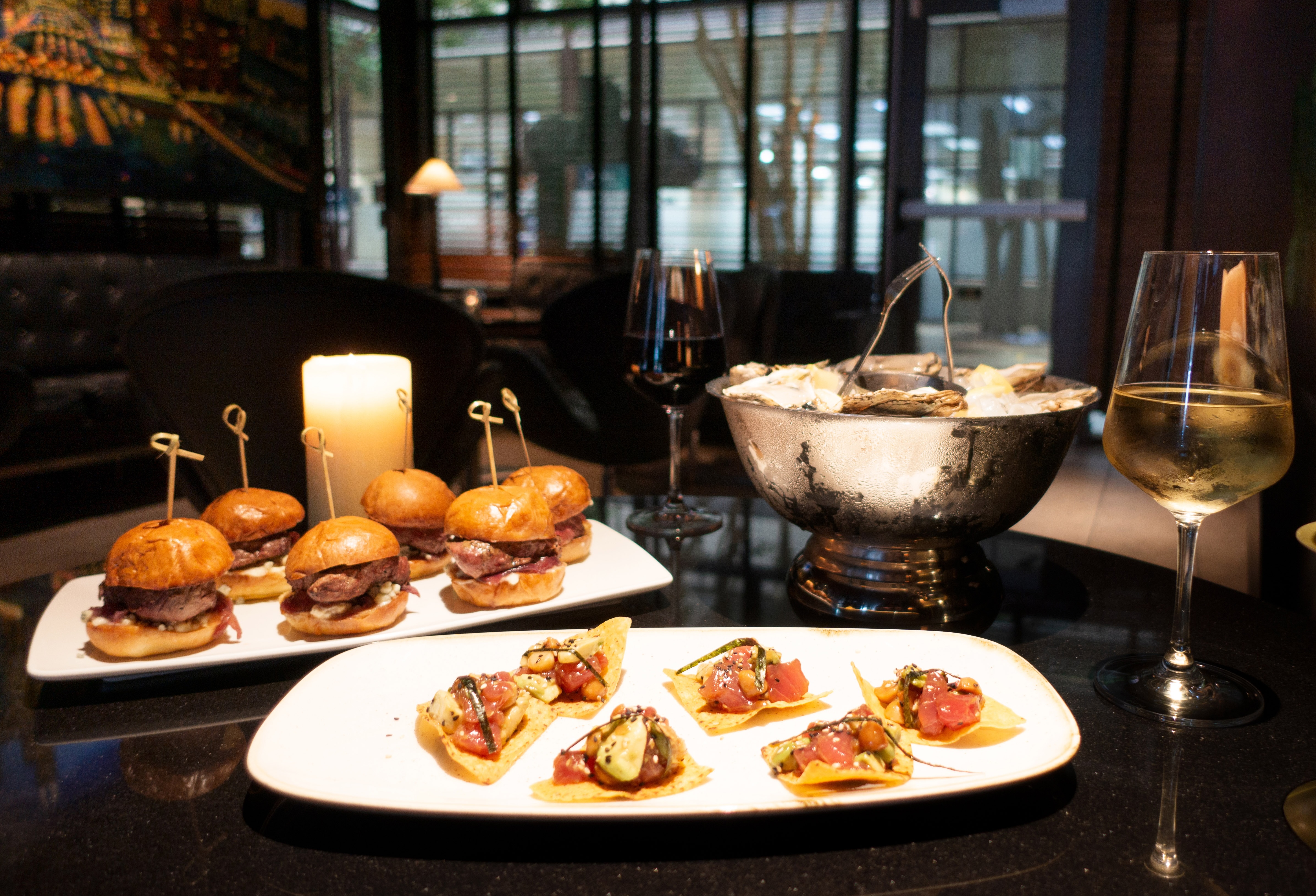 A table with sliders, ahi tuna bites, and a glass of wine