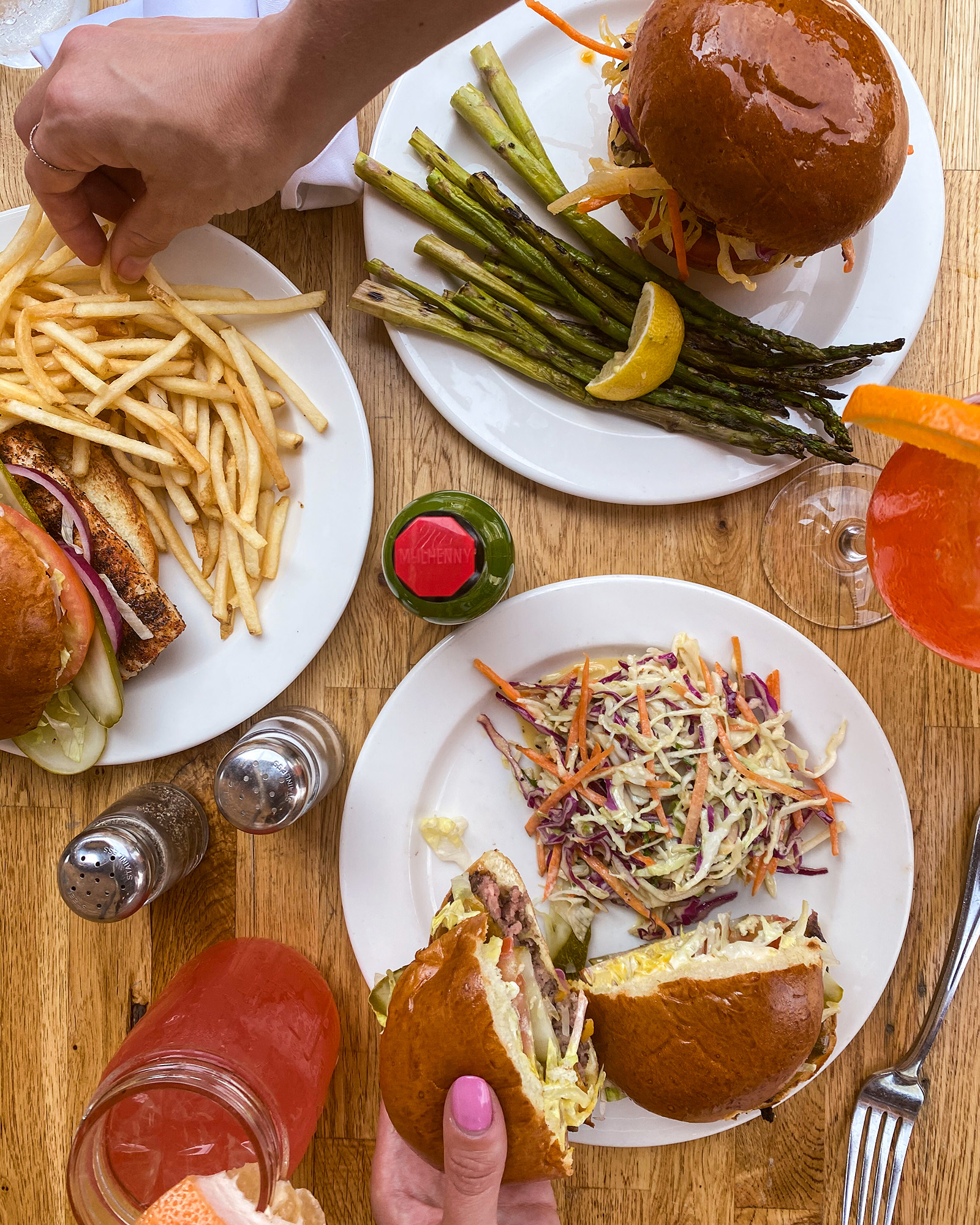 Overhead view of a table set with plates - a burger, turkey burger, and mahi mahi sandwich, plus sides and drinks
