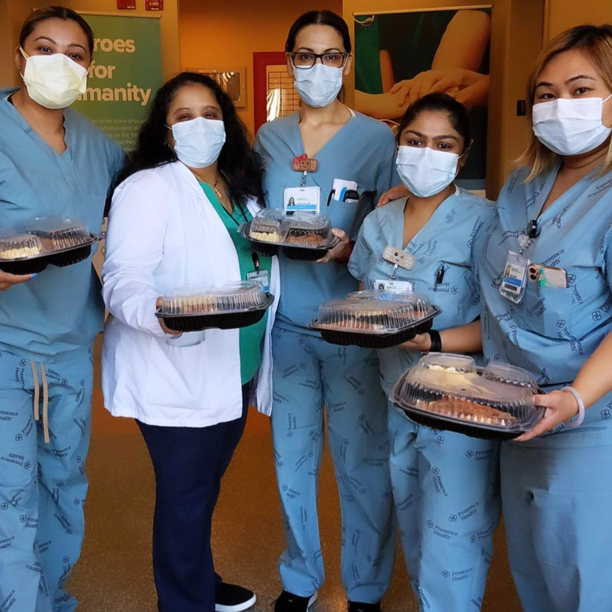 A group of nurses in scrubs smiling and holding boxed lunches