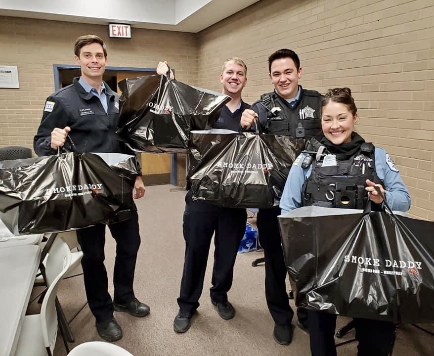 A group of police officers smiling while holding large catering bags from Smoke Daddy