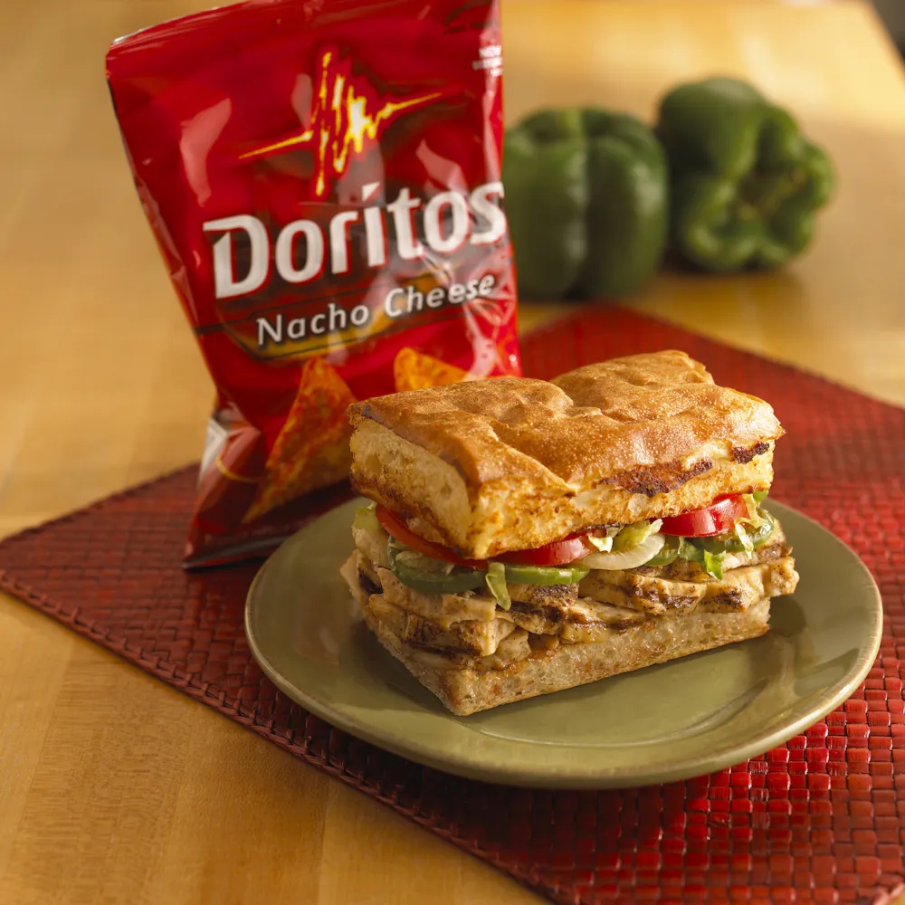 a sandwich on a plate next to a bag of chips