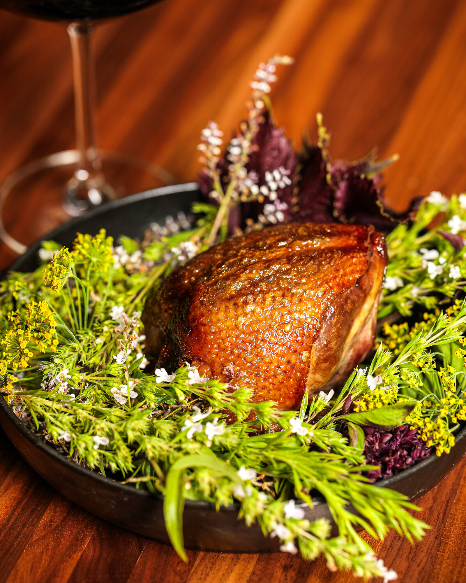 A whole roasted bird served in a cast iron pan nested in flowering herbs from the garden