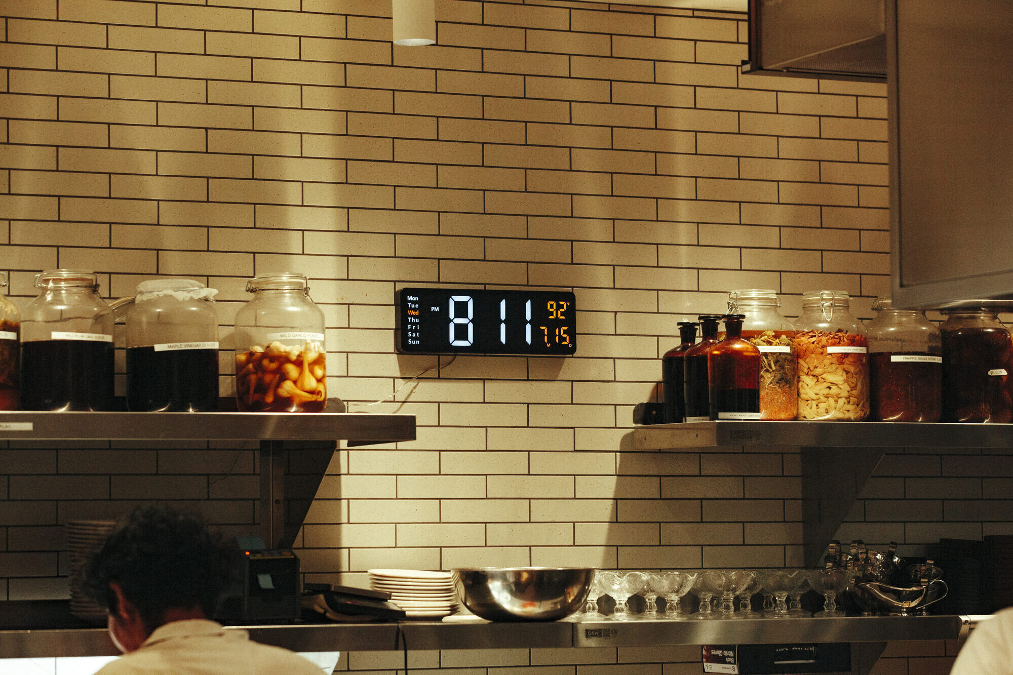The Folia kitchen in the evening, shelves lined with jars of wild garlic honey, maple vinegar, and preserved fruit