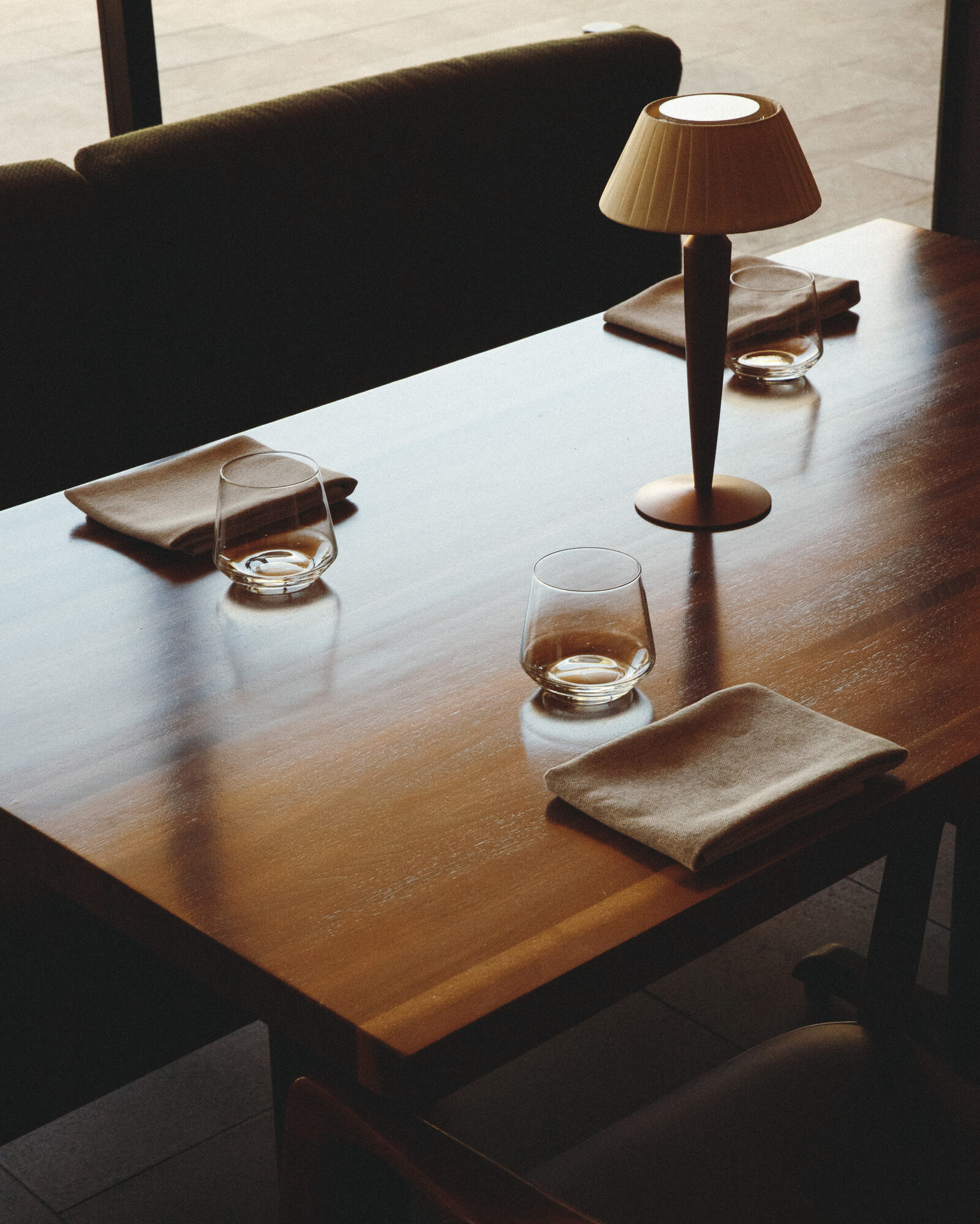 A set table at Folia with folded linen napkins, stemless glasses, and a small shaded lamp in afternoon light
