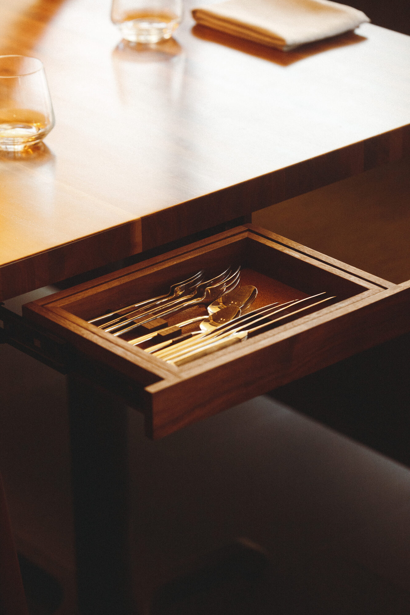 A drawer built into the dining table pulled open to reveal forks and spoons in a fitted walnut tray
