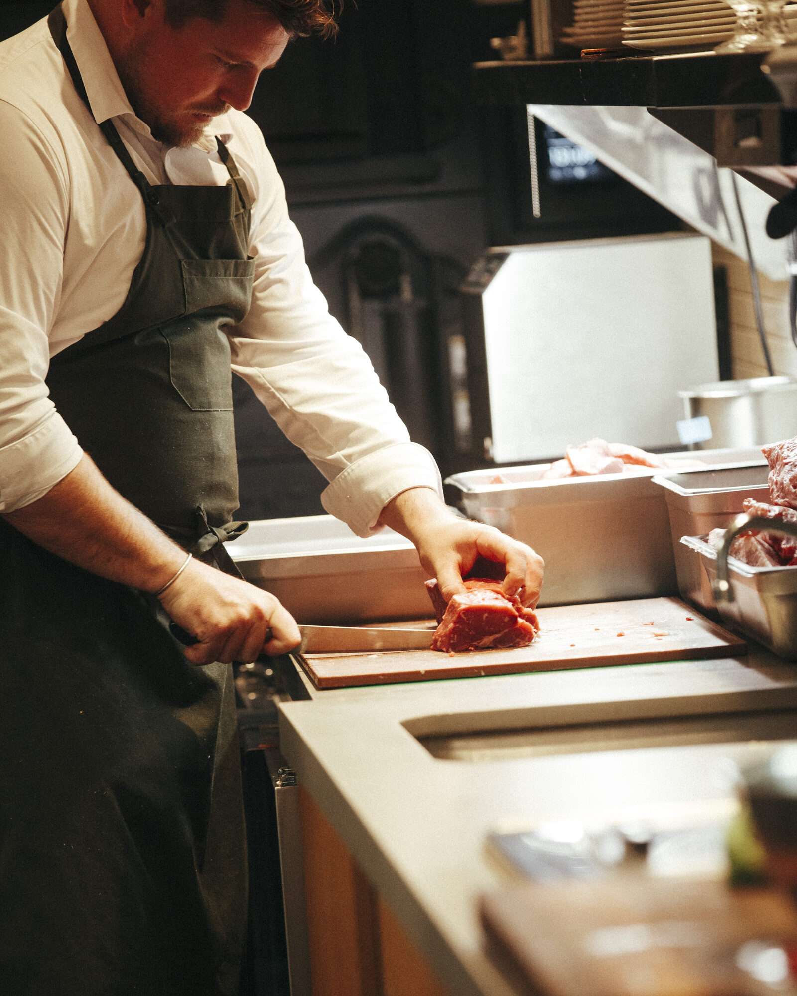 A chef portioning beef on a board at the pass in the Folia kitchen
