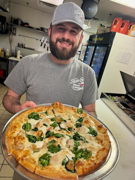 a man standing in front of a large pizza