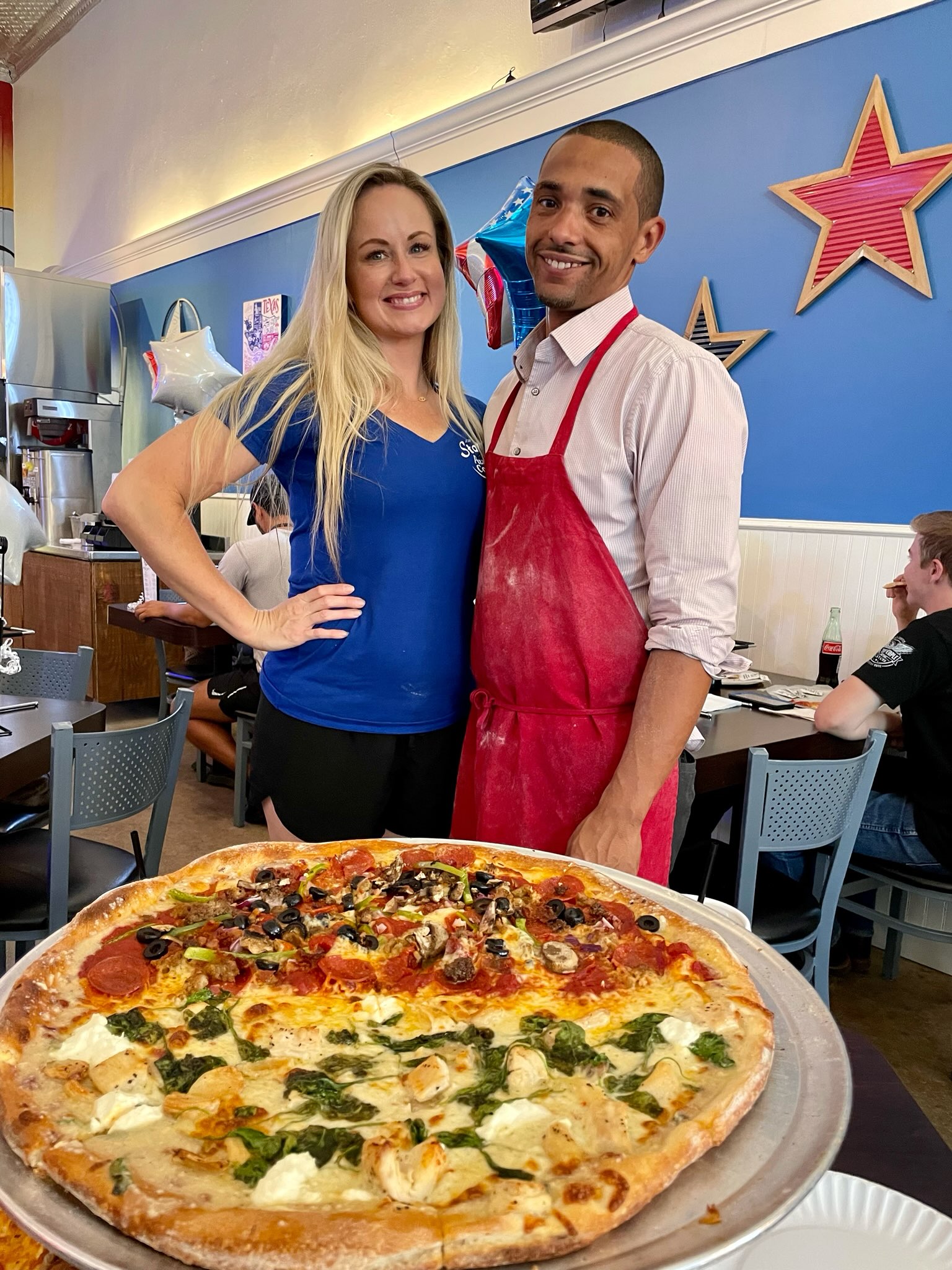 a man and a woman standing in front of a large pizza