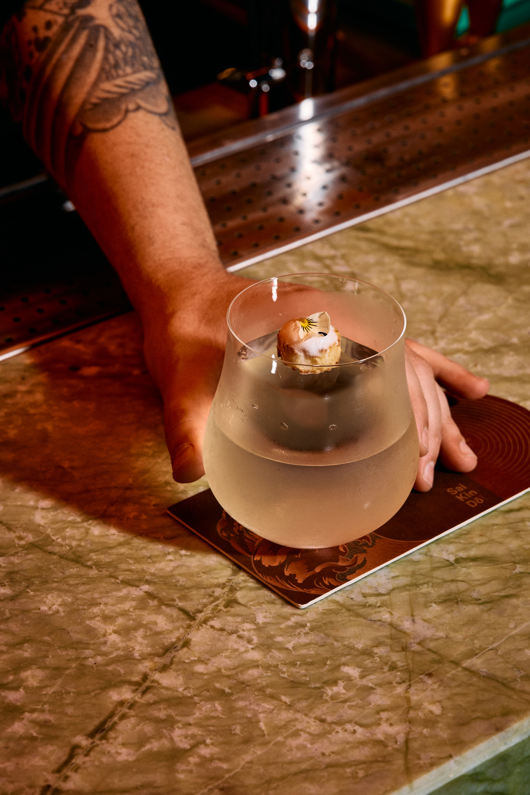 a hand holding a glass of liquid with a small piece of food on top