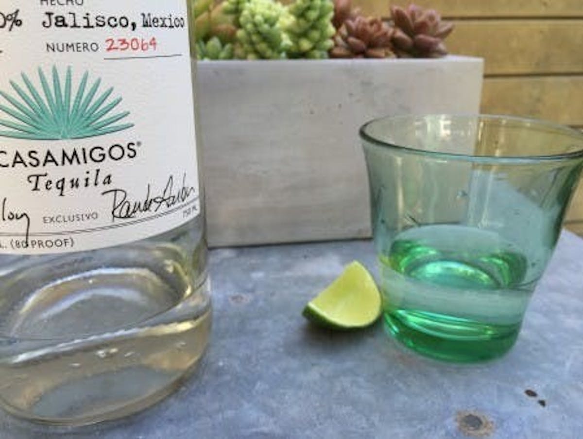 a glass with tequila served beside a bottle of casamigos tequila and a lemon