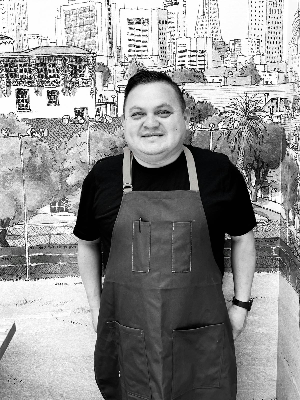 Short-haired man in black shirt and apron posing in front of camera