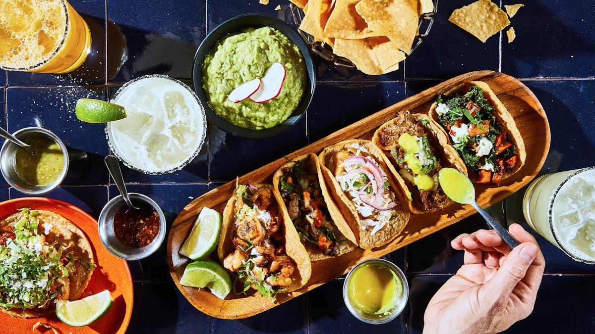 A spread of tacos served with guacamole, salsa, and lime wedges