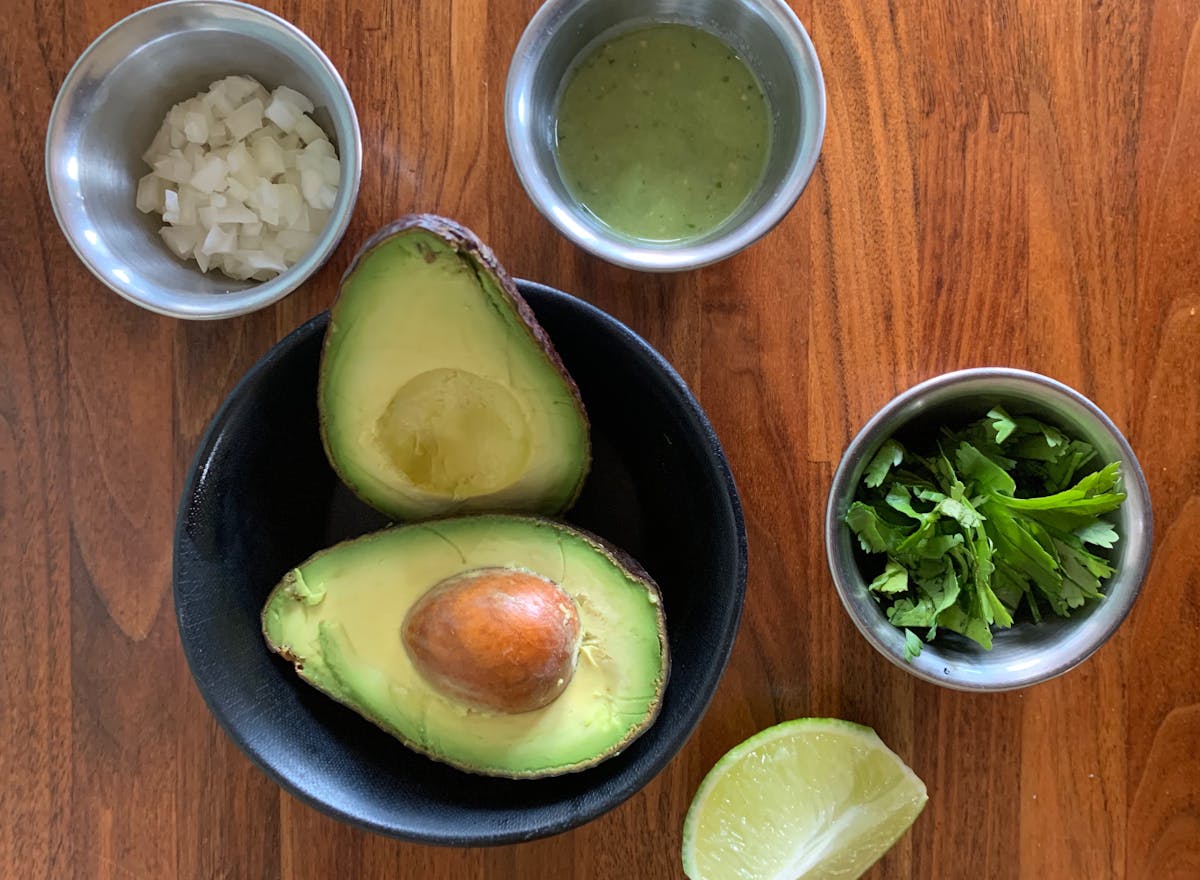 a bowl of avocado with accoutrements on top of a wooden table