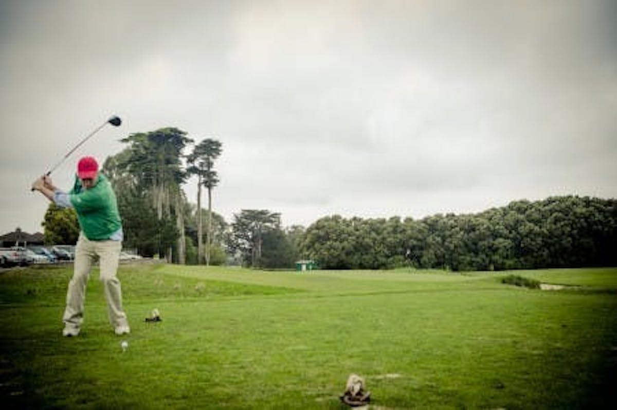 a man wearing a red cap, green shirt and white pants playing golf in a cloudy field