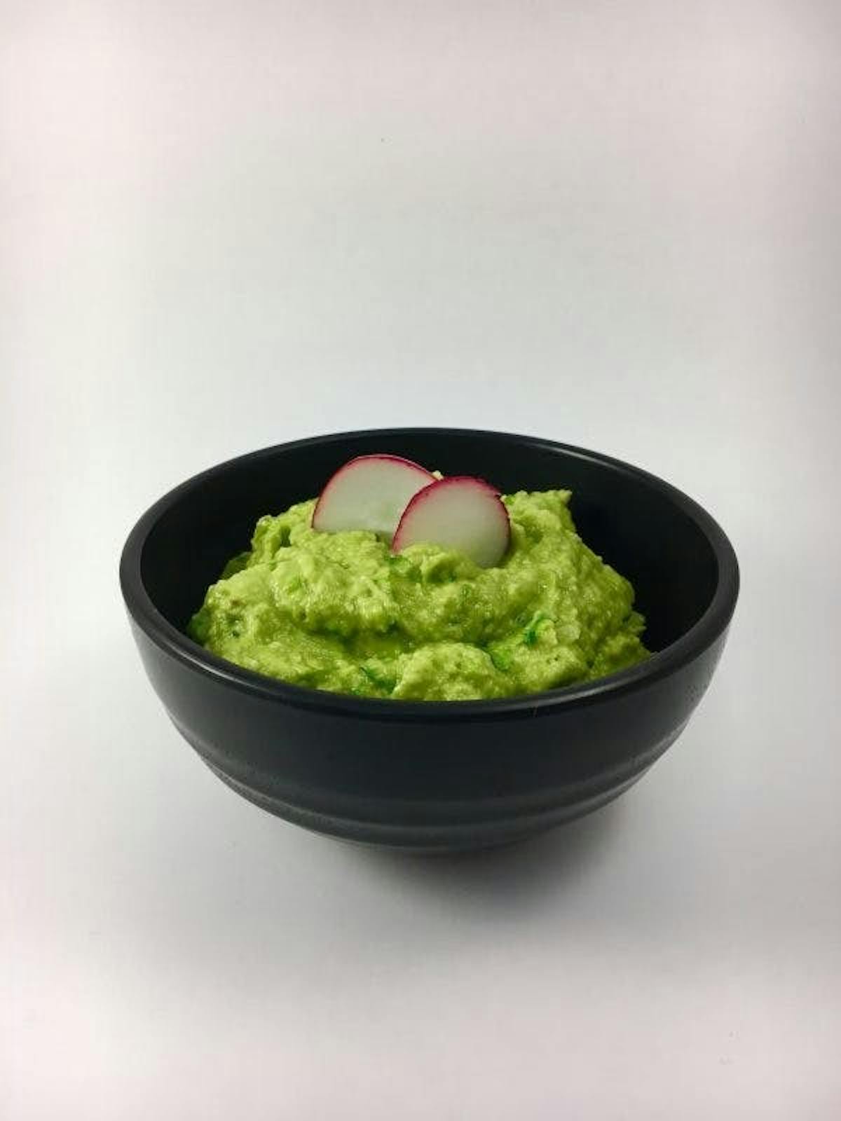 a bowl of guacamole and two slices of raddish on top