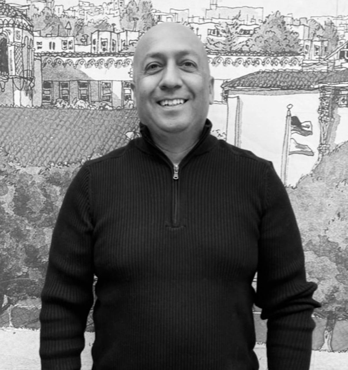 A man in a black sweater with a smile on his face, posing for the camera