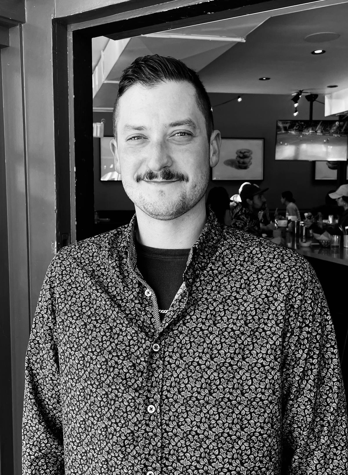 A man with a mustache and patterned shirt smiling at the camera