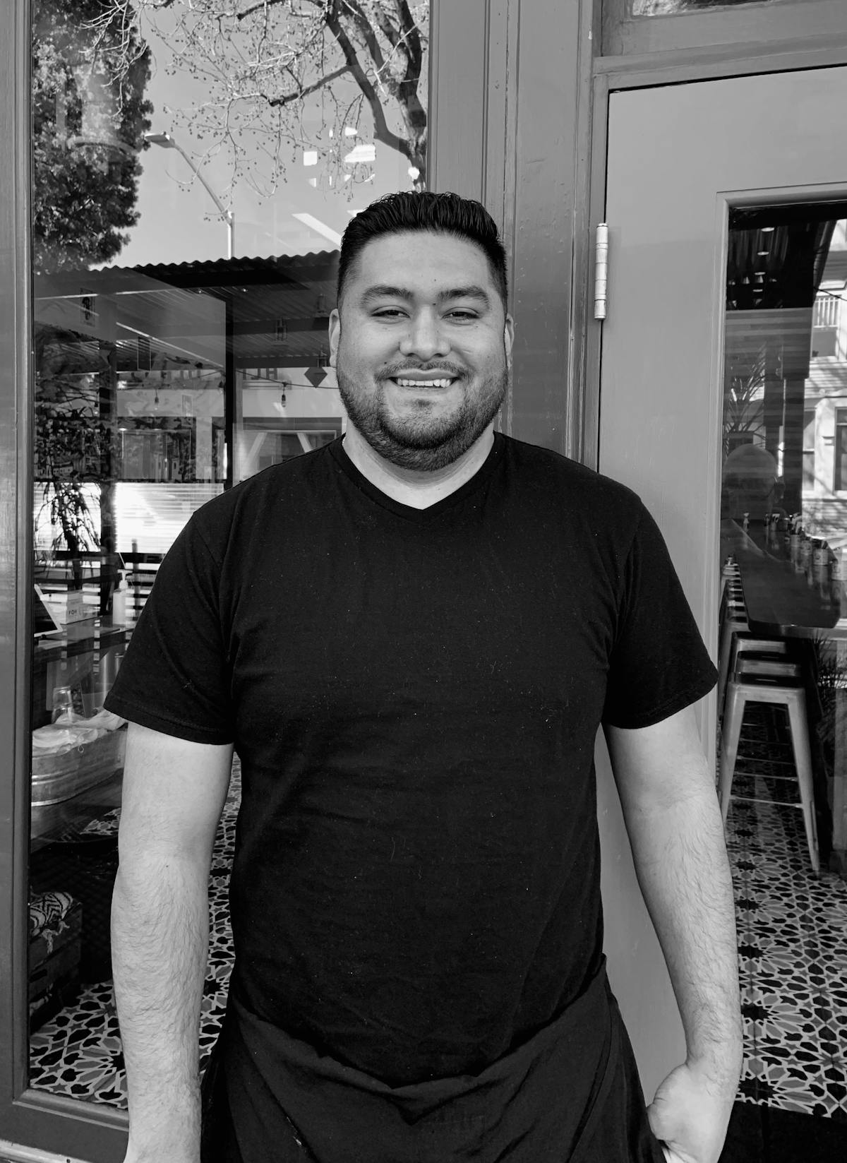 A man with short hair wearing a black shirt smiling in front of the camera