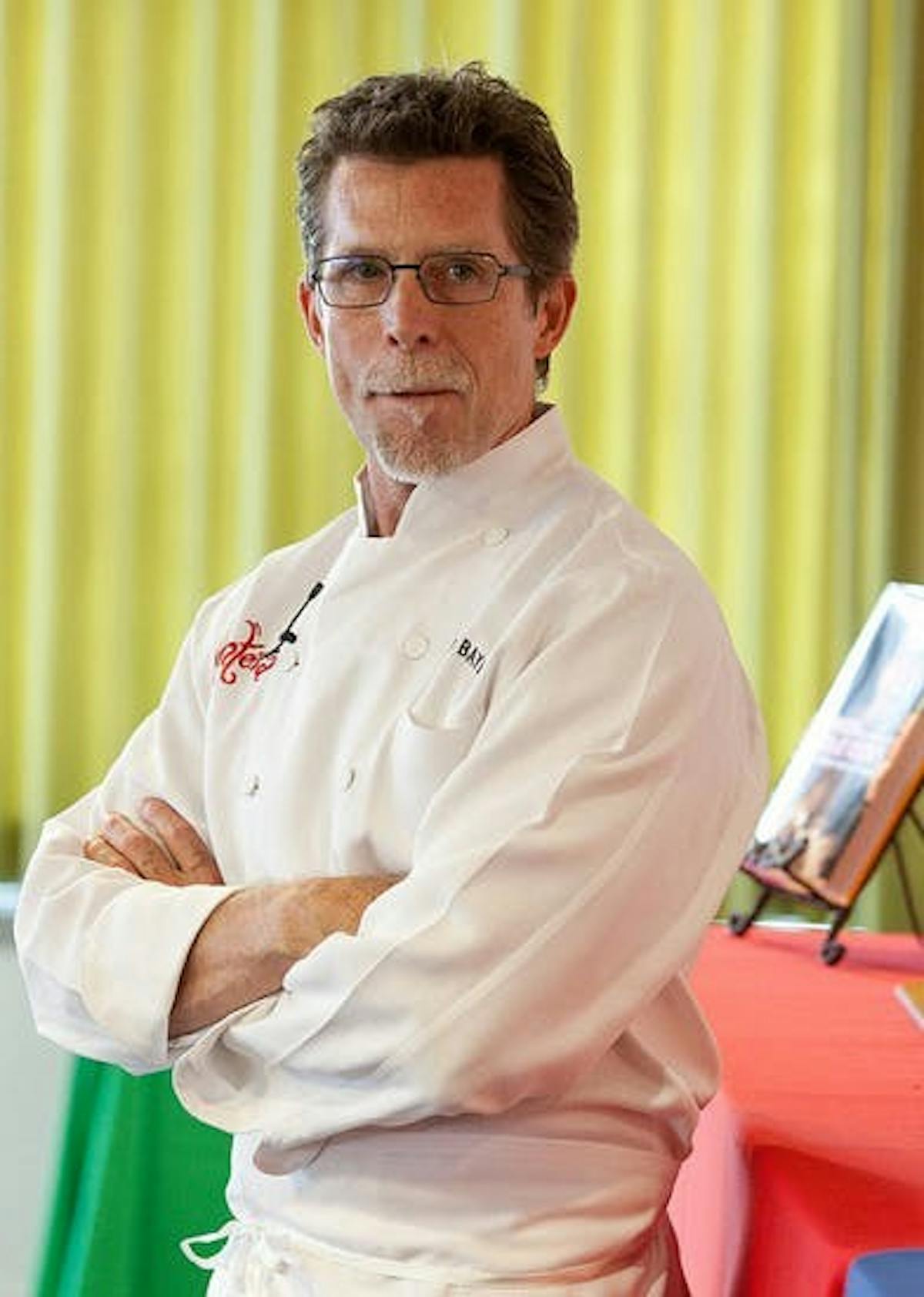 A man posing with arms crossed wearing a chef uniform