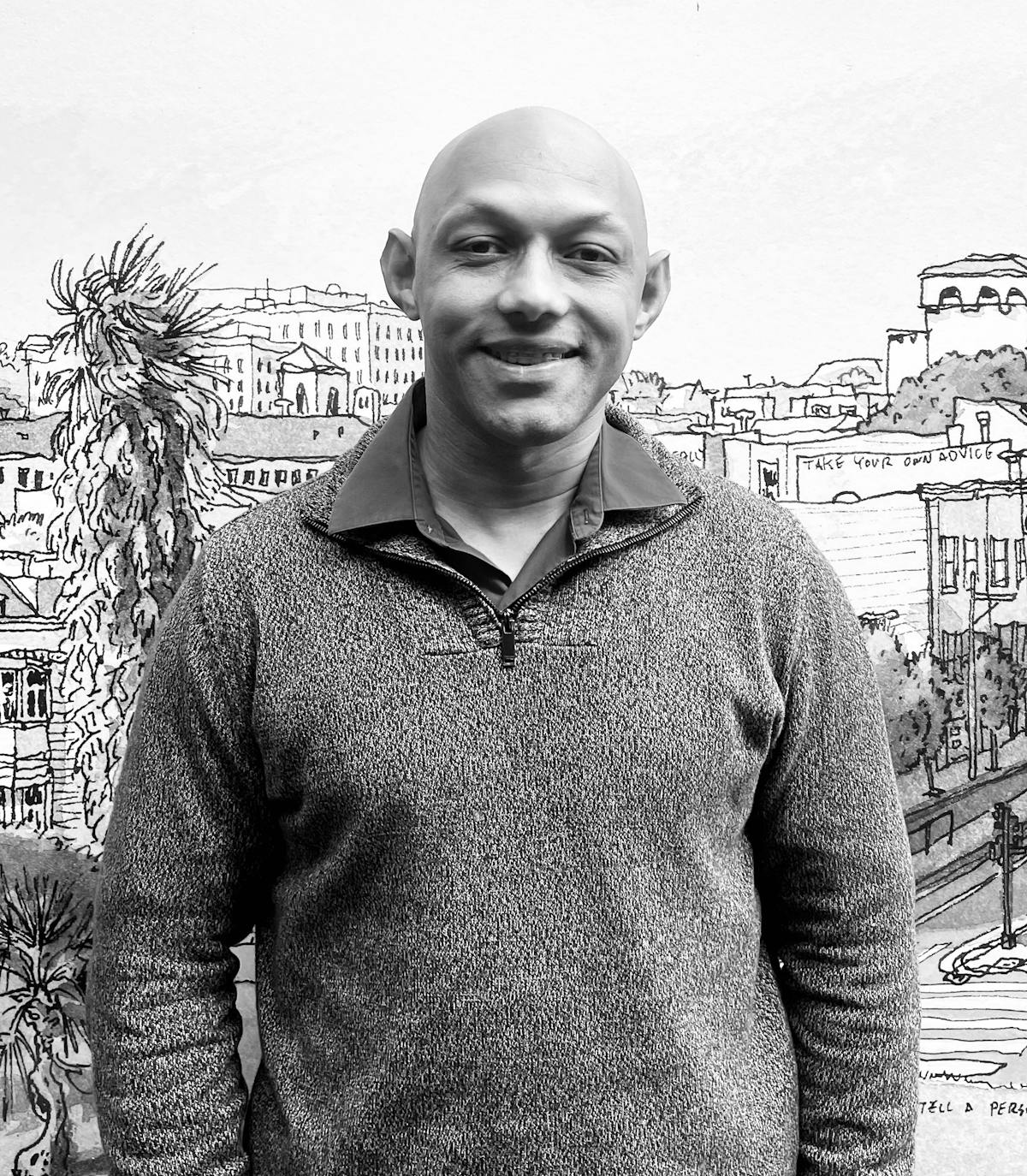 A man wearing a gray sweater smiling at the camera